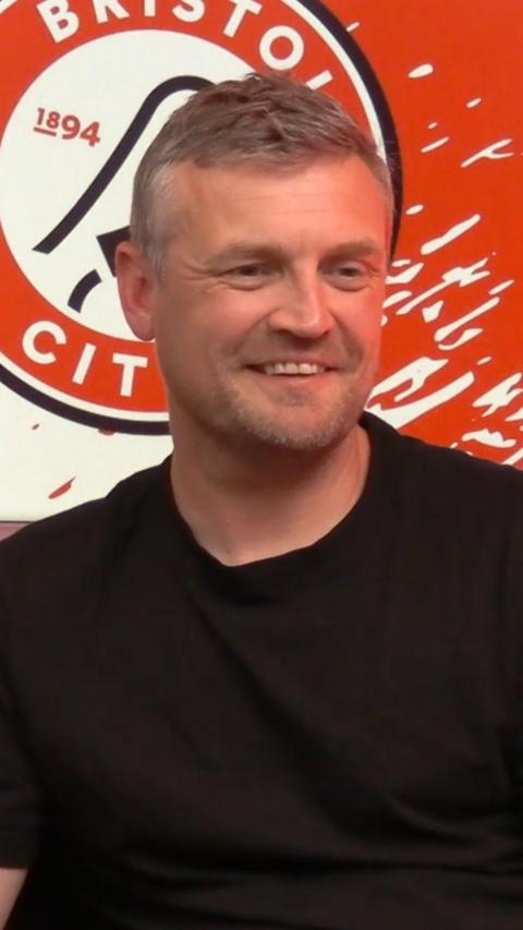 Michael Skubala standing in front of a red Bristol City logo. 