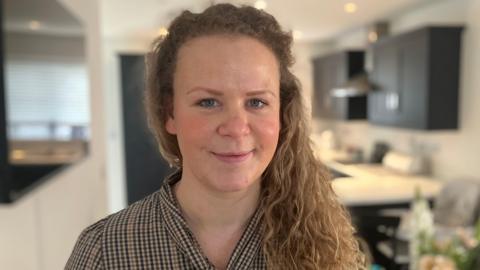 Anna Foster looking at the camera with a kitchen in the background.