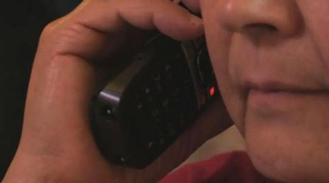 A man holds a phone handset to the side of his. We cannot see all of his face.