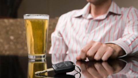 A car key on the table in front of a pint of beer and a man