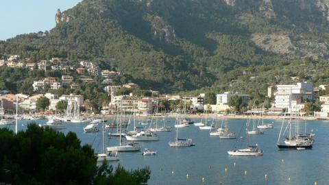 A bay filled with boats with large rocky cliffs covered in greenery in the background in Majorca