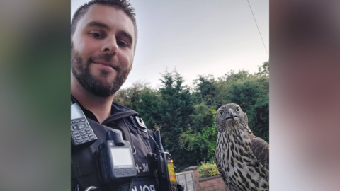 A police officer posing for a photo with a shocked bird of prey on his arm