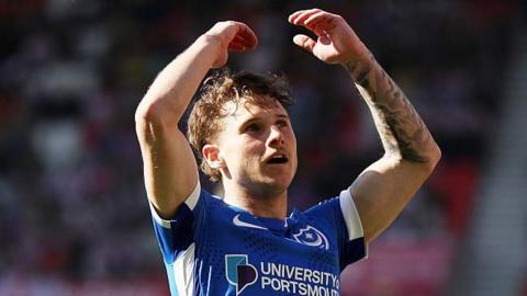Adrian Segecic wearing a blue Portsmouth match shirt with his arms raised in the air