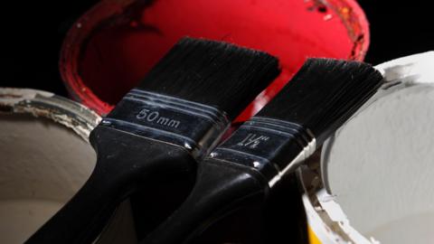 Two paint brushes sit balanced on paint cans. 