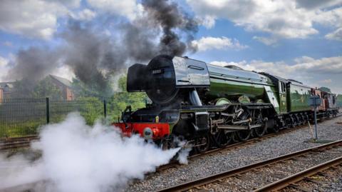 Smoke and steam surrounds a green locomotive engine