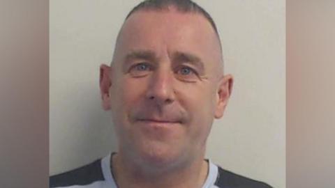 Police picture of Nigel Mullan, who has short brown hair and it wearing a black and white T-shirt.