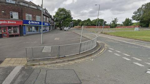 Muirhead Avenue in West Derby showing a row of shops and trees lining the road and traffic lights