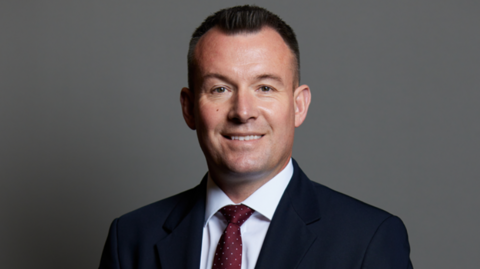 Stuart Anderson wearing a dark suit and red tie