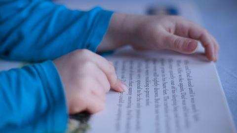 A white boy's hand following text from a children's book