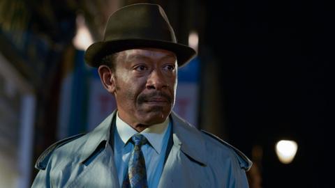 A man standing outside at night with a hat looking off camera