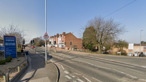 A junction with a Tesco Express sign on the left. There is also a school crossing patrol sign