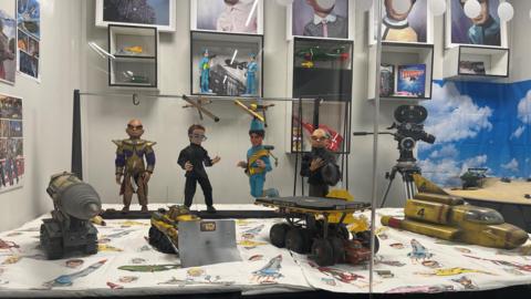 Puppets from Thunderbirds behind glass alongside other memorabilia from the show