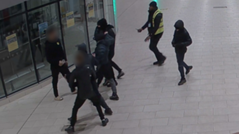 Teenagers. all clad in black with their faces covered, tussle in a shopping centre as a security guard moves in
