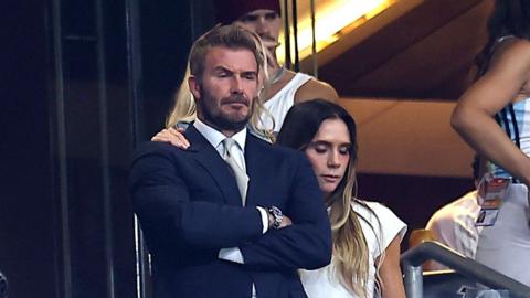 David Beckham appears emotional with arms hands crossed following England's semi-final defeat. His wife Victoria has an equally sad expression and consoles him with an arm on his shoulder
