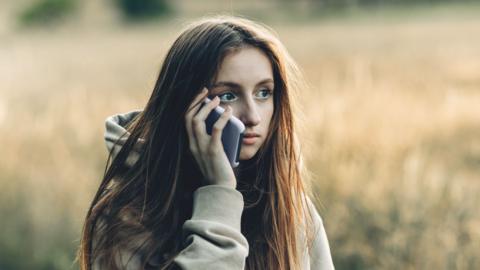 A teen girl holds her mobile phone to her ear with a panicked and shocked look on her face.