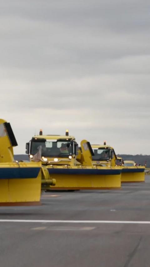 Three yellow de-icers on an airport runway.
