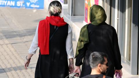 An Iranian woman without a mandatory headscarf, or hijab, walks in a street in Tehran, with another woman who is wearing a hijab.