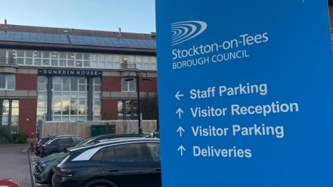 Dunedin House, Stockton Council's headquarters on Columbia Drive, Thornaby. A large blue sign guides people to the visitor reception.