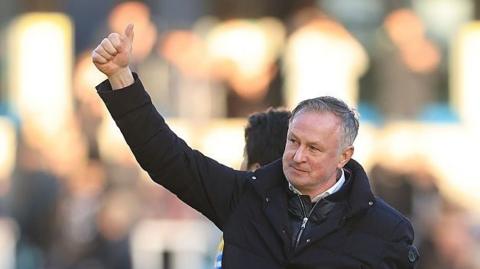 Blackburn Rover boss Michael O'Neill with thumb up in the air at fans smiling, wearing dark blue winer jacket