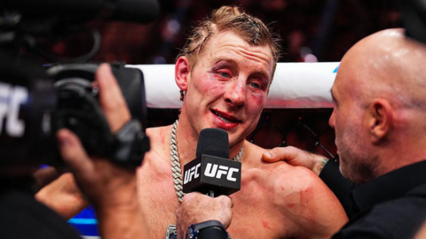 A brusied Paddy Pimblett speaks on the UFC mic. He has blood stains on his face and his eyes are red.