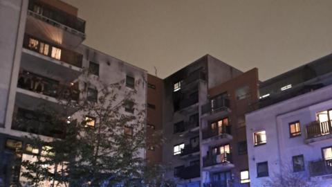 A block of flats with the flat on the fifth floor covered with black smoke and soot.