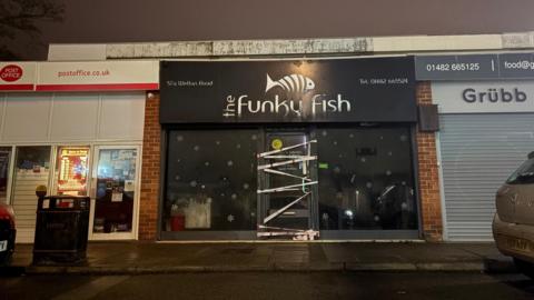 A fish and chip shop, with tape around the doors preventing entry. The sign is blackened.