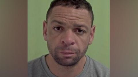Doherty's police mugshot. He has short dark hair and stubble and is wearing a grey sweatshirt.