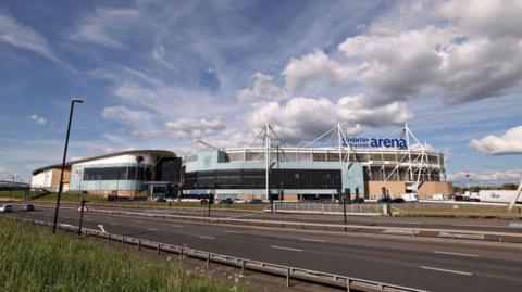 The outside of the Coventry Building Society Arena, with several road lanes and grass in the foreground
