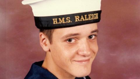 Simon Parkes smiles at the camera in a portrait photo. He wears a navy uniform with an HMS Raleigh cap