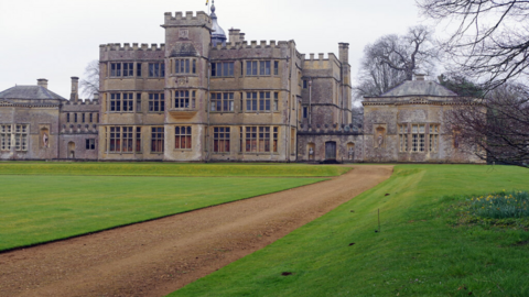 A grand three-storey house with turrets, behind a bowling green