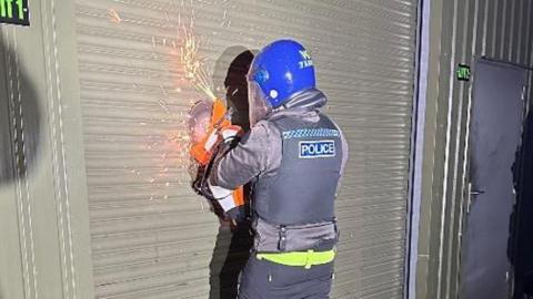 A police officer cutting into a metal shutter in order to get into a storage yard.