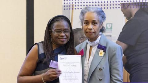 Pretty Manyimo in a blue and grey dress next to another woman in a pastel blue suit