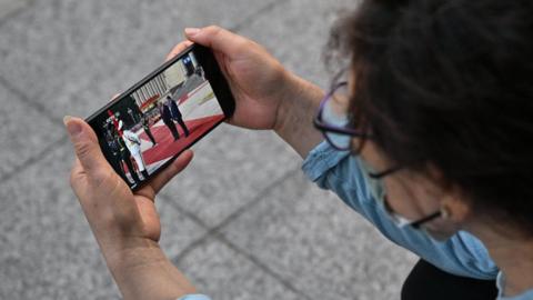 A woman watches a video of US President Donald Trump with China's President Xi Jinping on a mobile phone in Beijing, in May this year