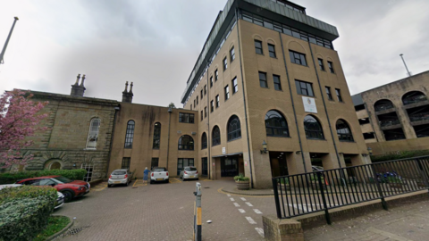 A council office building of more than four storeys is pictured. On the ground level is a car park with cars parked in spaces.
