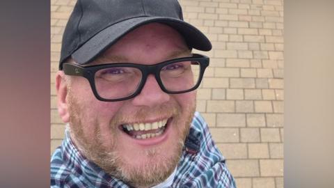 Damien Paul Bintley, a man with a beard, dark glasses and a black cap.
