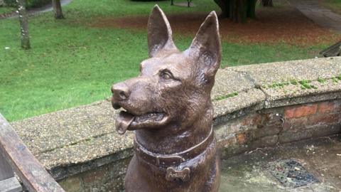 A bronze statue of a German Shepherd dog wearing a collar with a name tag that reads “Antilly".