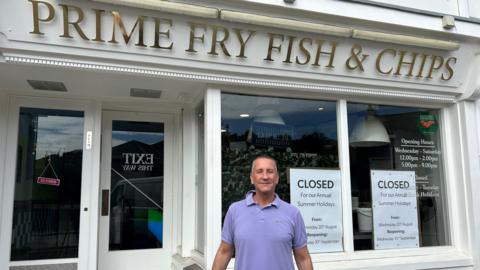 Tom Howell is stood in front of his shop Prime Fry Fish & Chips wearing a purple polo shirt.