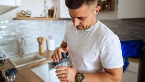 A young man in a white t shirt with a protein shake