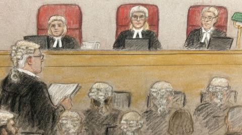 A court sketch shows three judges sitting in red chairs overlooking a courtroom; a lawyer before them reads over a document