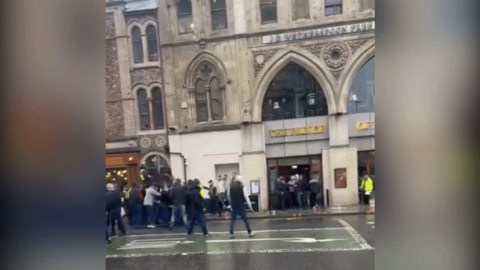 A frame from a video shows a group of people stood on the road and pavement outside the Prince of Wales pub in Cardiff. There are more people gathered in the doorway of the pub.