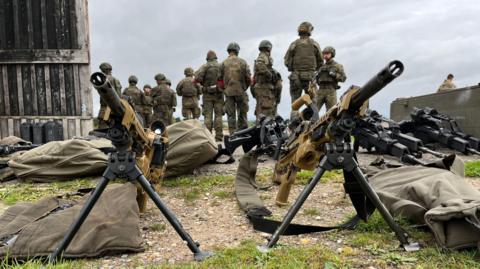 Two guns pointing in the air, with soldiers stood in the background