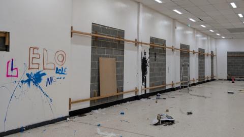 The inside of The Market Gallery. Graffiti has been painted and paint smeared onto the white walls. Rubbish is scattered on the floor and much of the walls are bare of artwork.