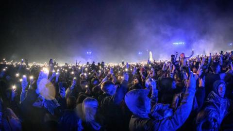 A crowd of people at night lit up in blue light from a stage.