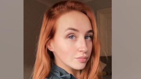 A woman with red hair and blue eyes smiling. 