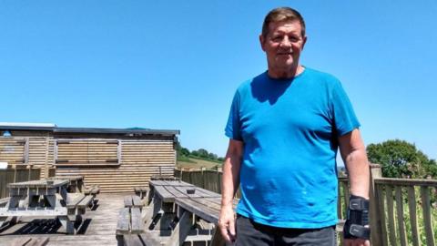 Gary Bulmer stood on the pub decking. He has brown hair, wearing a blue T-shirt and looking directly into the camera