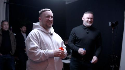 Luke Littler and Wayne Rooney smile as they play darts