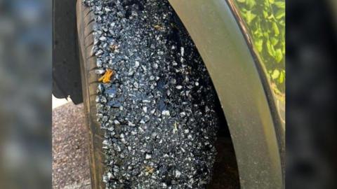 A car tyre that has been covered in small rocks and a black gooey substance. 