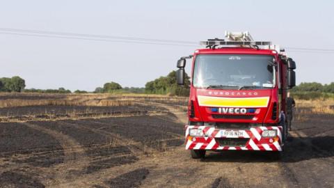 A fire engine is parked on a piece of scorched, burnt, brown farmland.