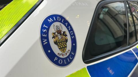 A blue, white and yellow West Midlands Police emblem on the rear of a police car. 