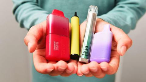 A child holds four single-use vapes in their palms.